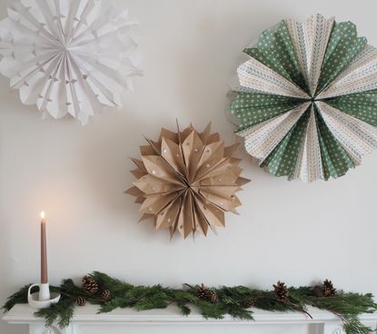 Christmas paper bag decorations on a wall above mantel, foliage on mantel, pine cones, single lit candle 