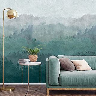 A mural of mountains and trees on a wall behind a sofa, coffee table and gold lamp