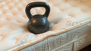 A black kettlebell placed on the edge of the Saatva Classic mattress during edge support testing