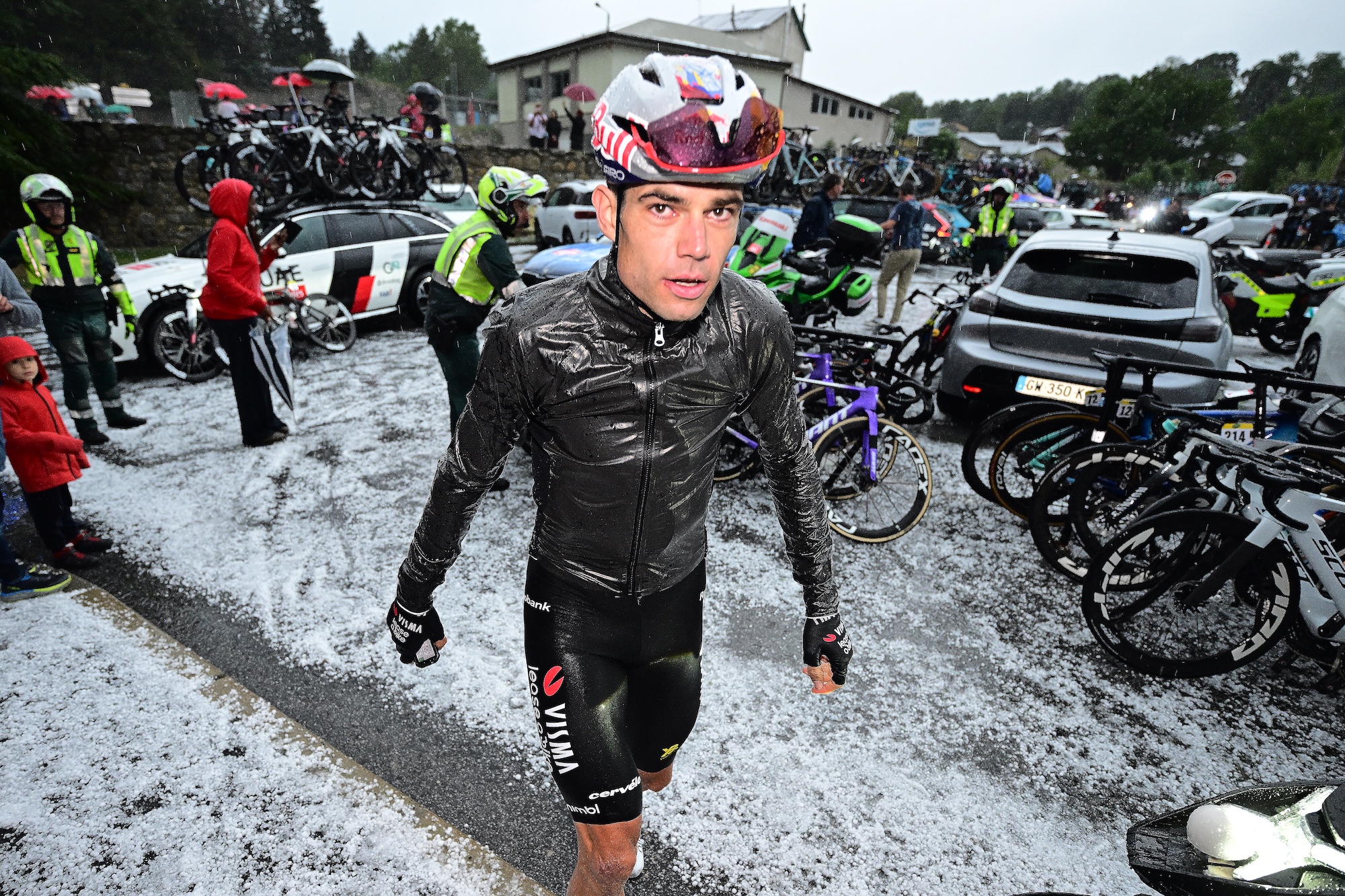 Wout van Aert hikes through the hail in the parking lot amid team cars and bikes