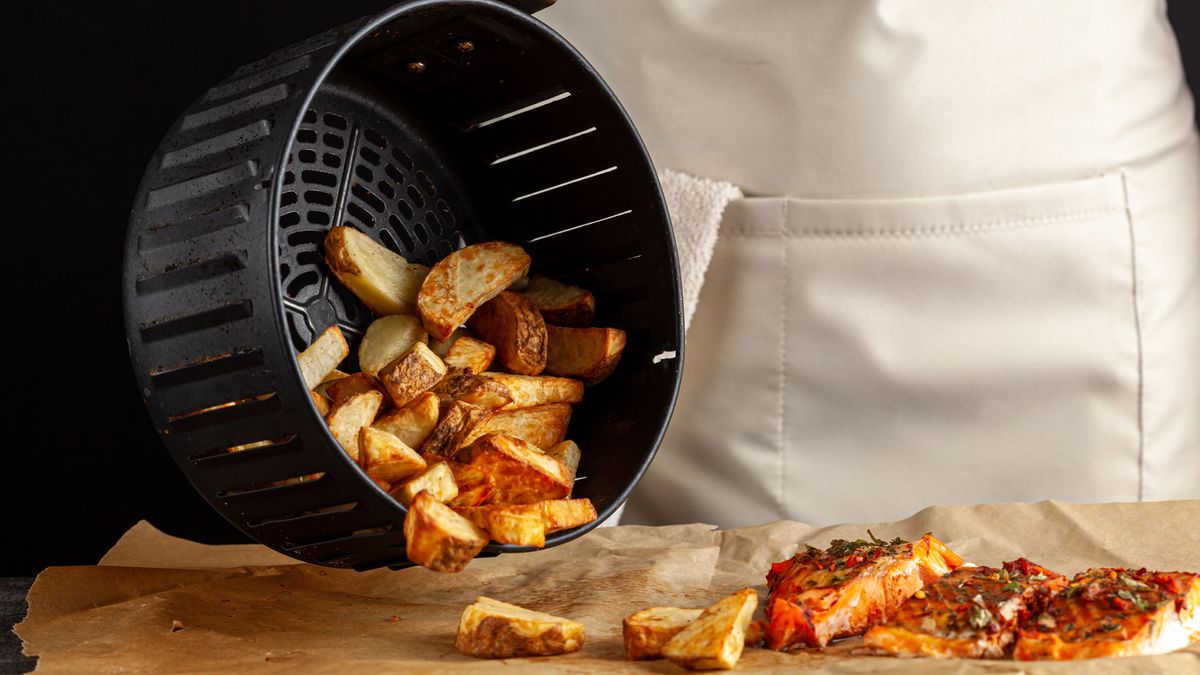 Potato wedges being tipped out of air fryer basket onto brown paper