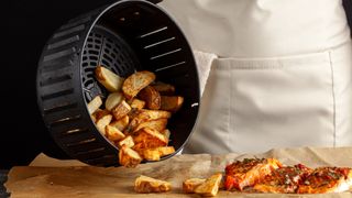 Potato wedges being tipped out of air fryer basket onto brown paper