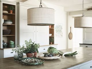 raffia drum pendant shade above kitchen island with wooden countertop, decorated with food and plates