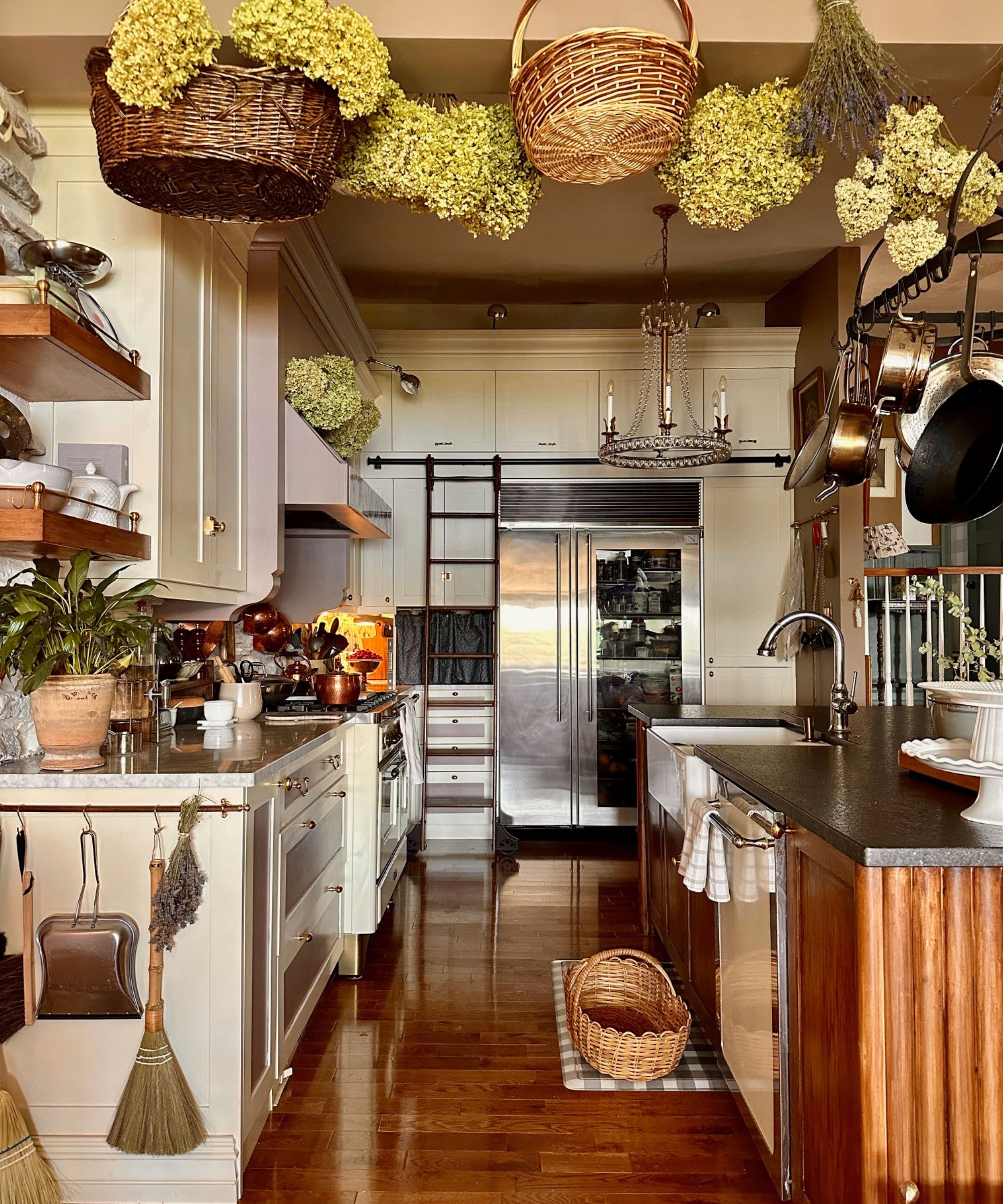 Kitchen with cream cabinetry, wood island, open shelves, pots and pans and baskets hanging