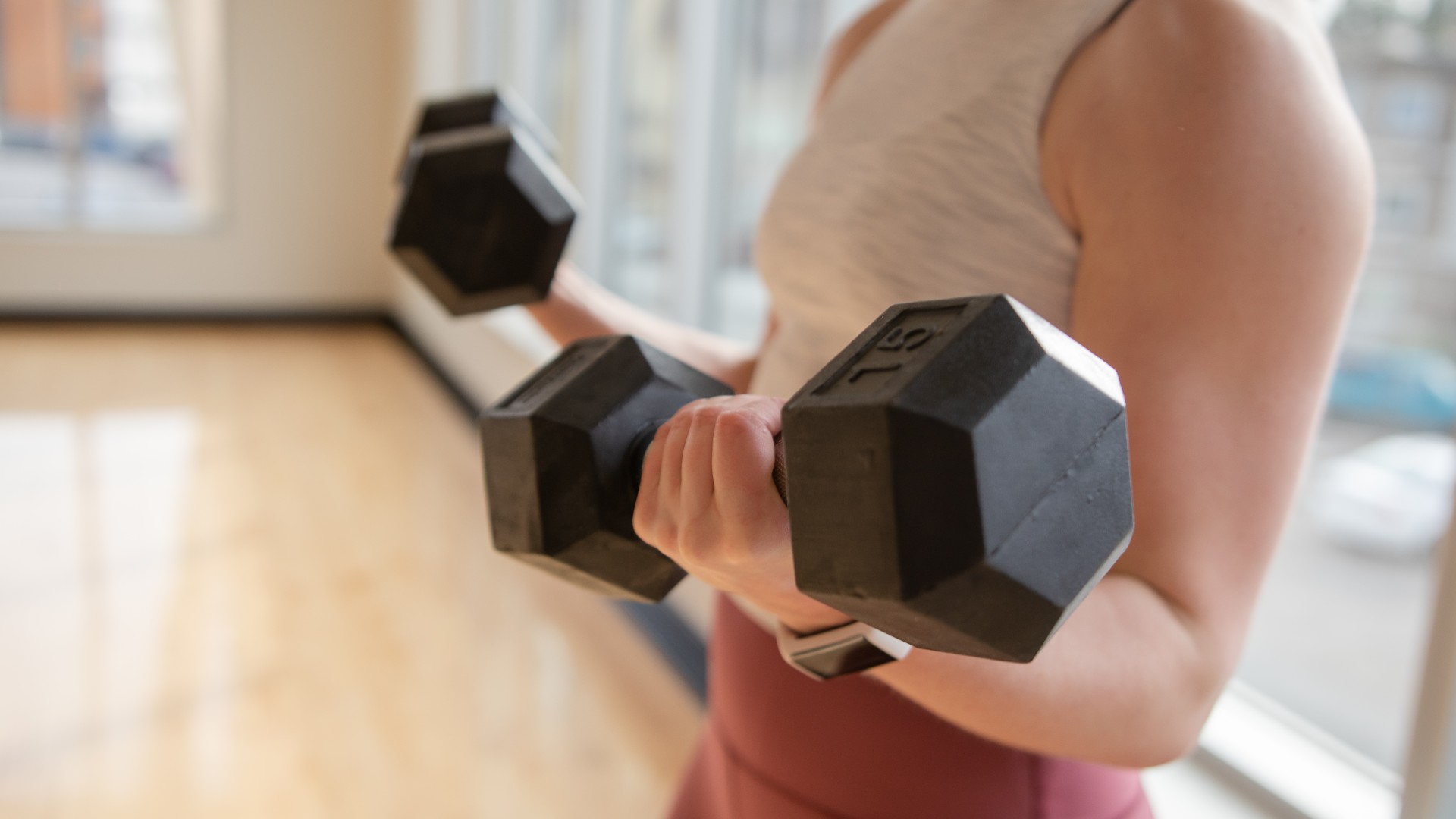 Person holding two dumbbells while curling biceps close-up