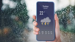 A phone showing a weather app with planned thunderstorms in front of a window covered in rain