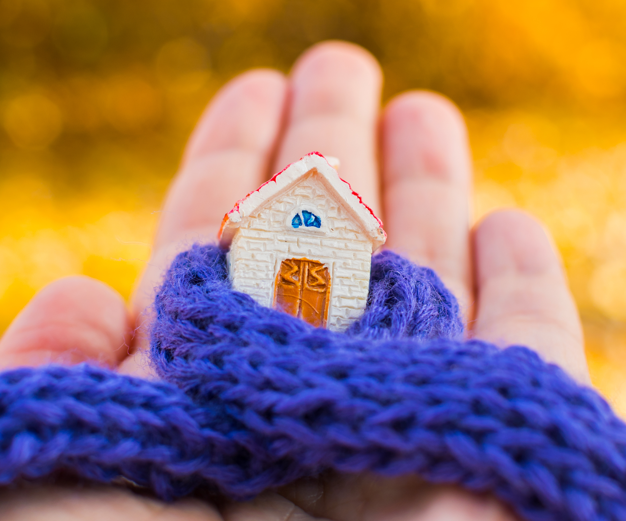 hand holding model of house wrapped in thin knitted blue scarf