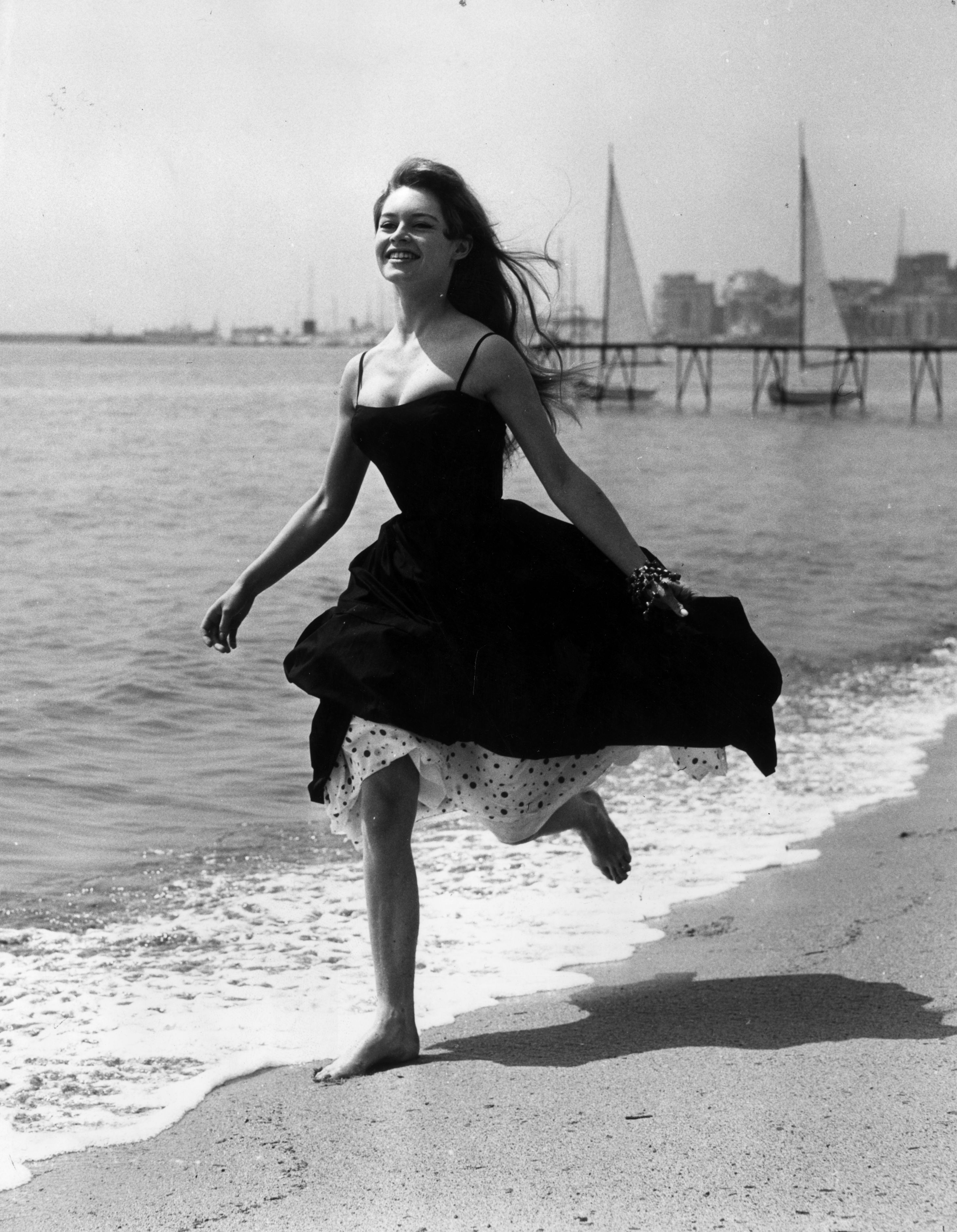 Brigitte Bardot runs on the beach wearing a midi dress at the Cannes Film Festival.
