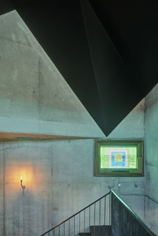Interior view of the stairwell at Pálás Cinema featuring concrete walls, a wall light, a black ceiling and a resin coated window