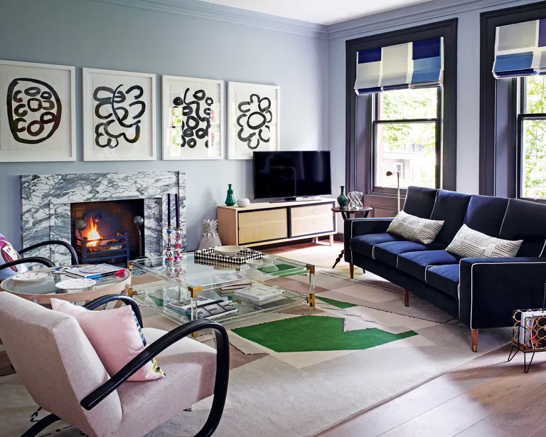 A living room with pale blue walls, a marble fireplace, dark blue sofa and pale pink armchairs