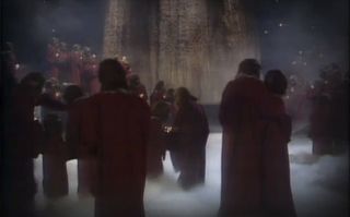 people in robes walk among fog in a wooded movie set