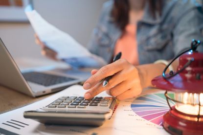 A woman uses a calculator while reviewing paperwork at her desk. 