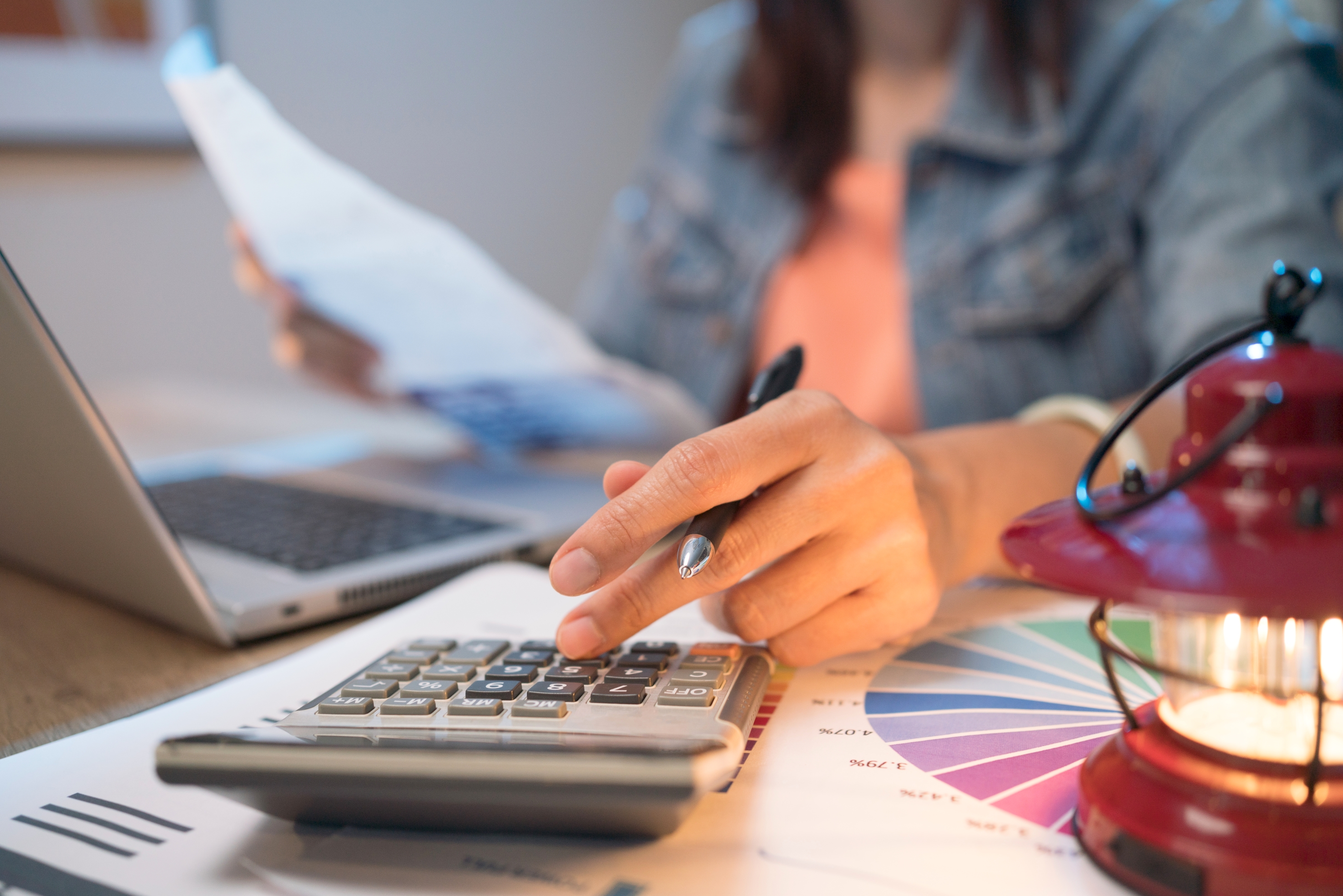 A woman uses a calculator while reviewing paperwork at her desk. 