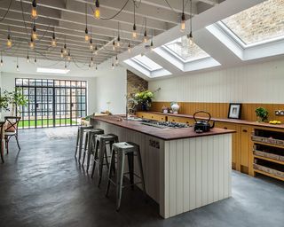 A large side return kitchen extension with glazed roof panels and a large wooden island with metal bar stools