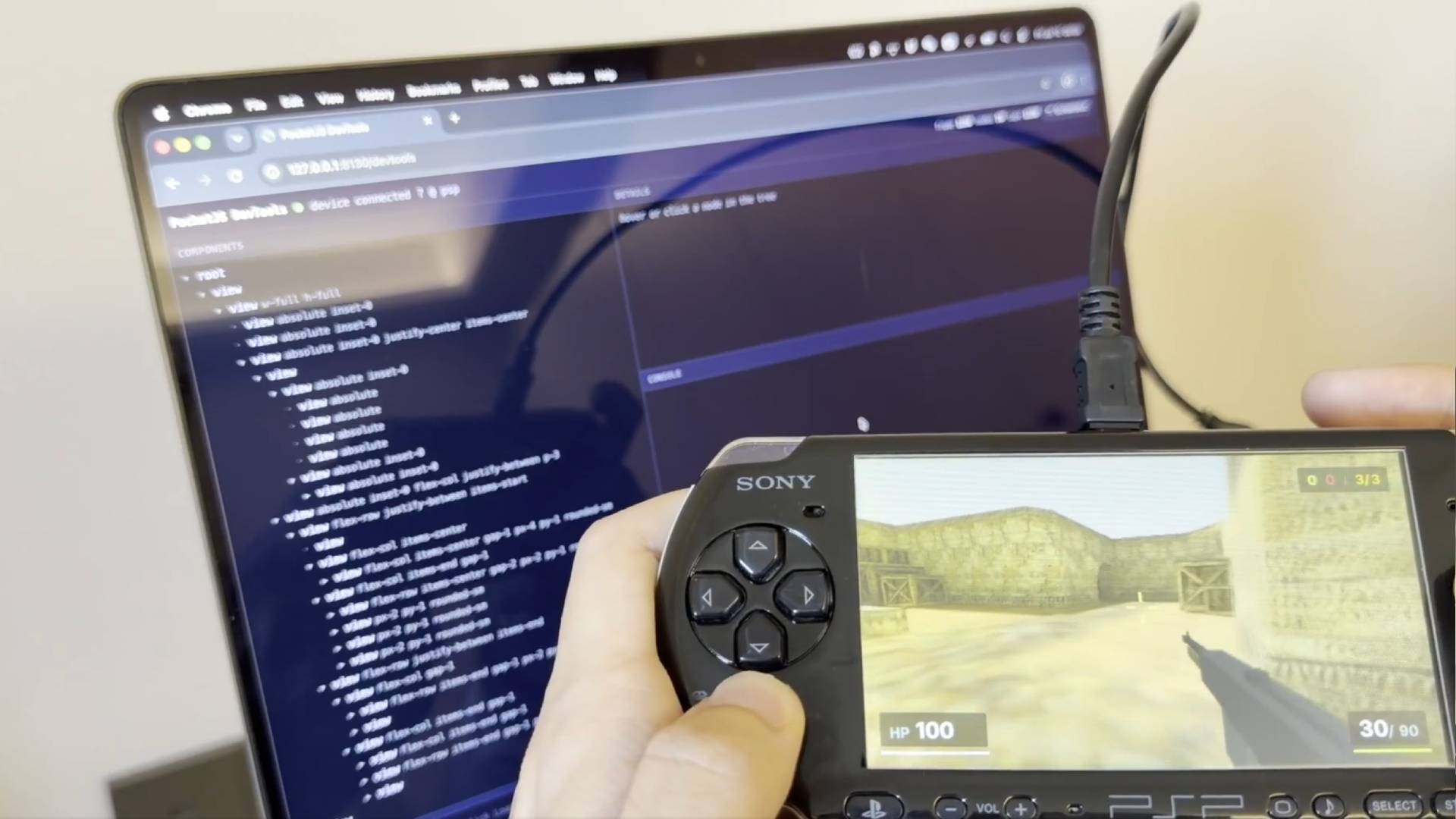 A developer plays a Counter-Strike clone on the original PSP. They have a laptop open, displaying development code.