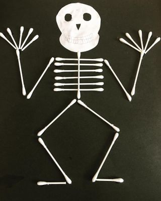 kids craft of making a skeleton out of ear buds on a black piece of paper