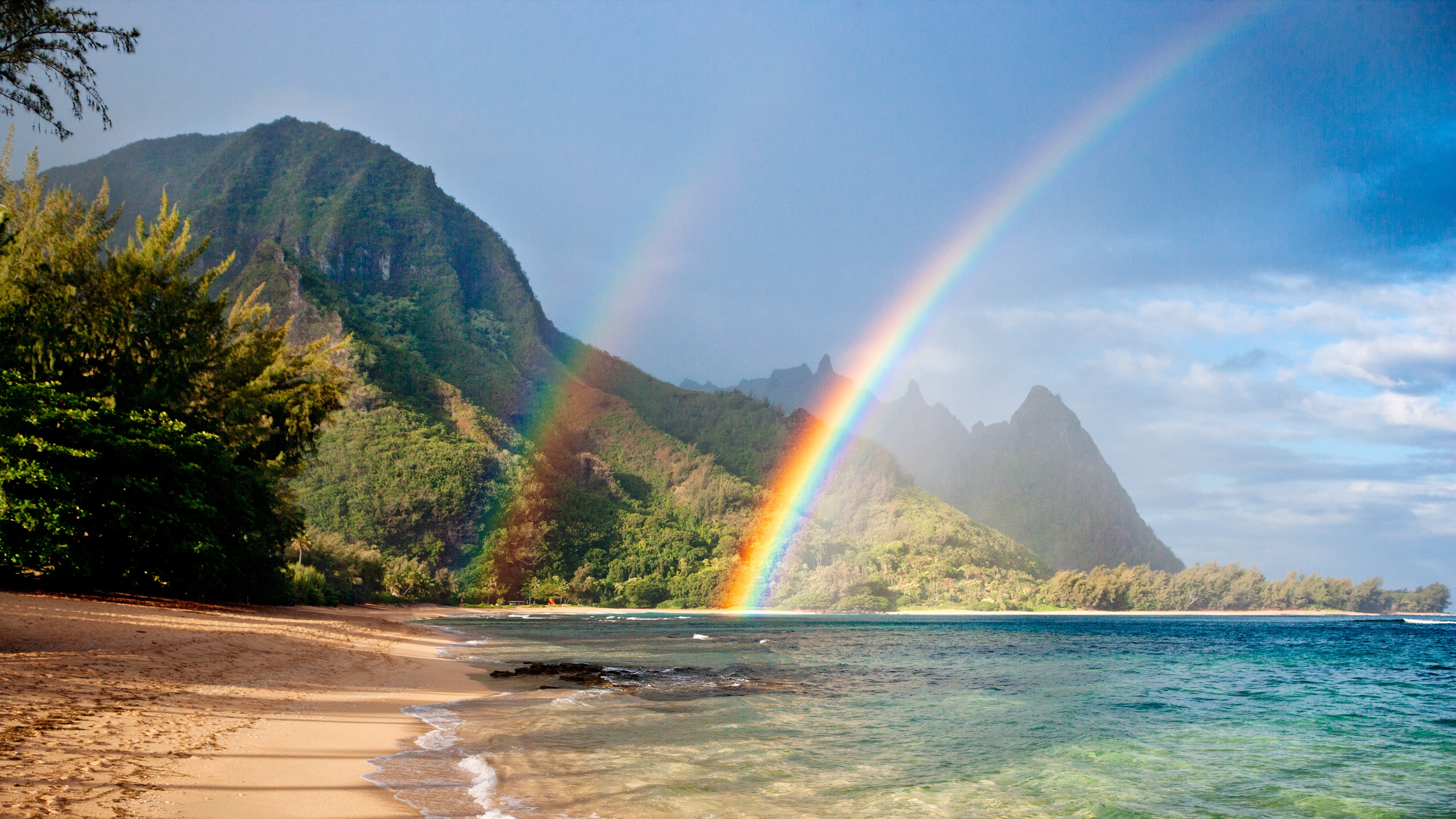 Double rainbows over a Hawaiian beach with mountains in the background.