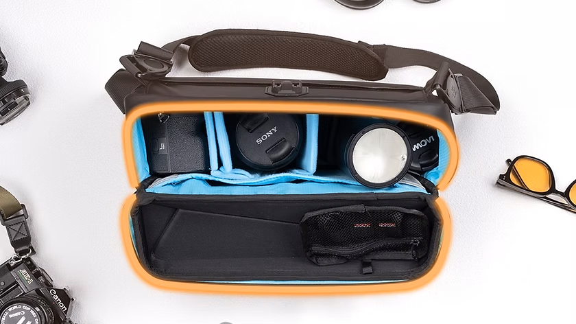 Open MagGo X camera bag with blue dividers, containing a Sony camera, lens, and a light; surrounded by accessories like watches and sunglasses