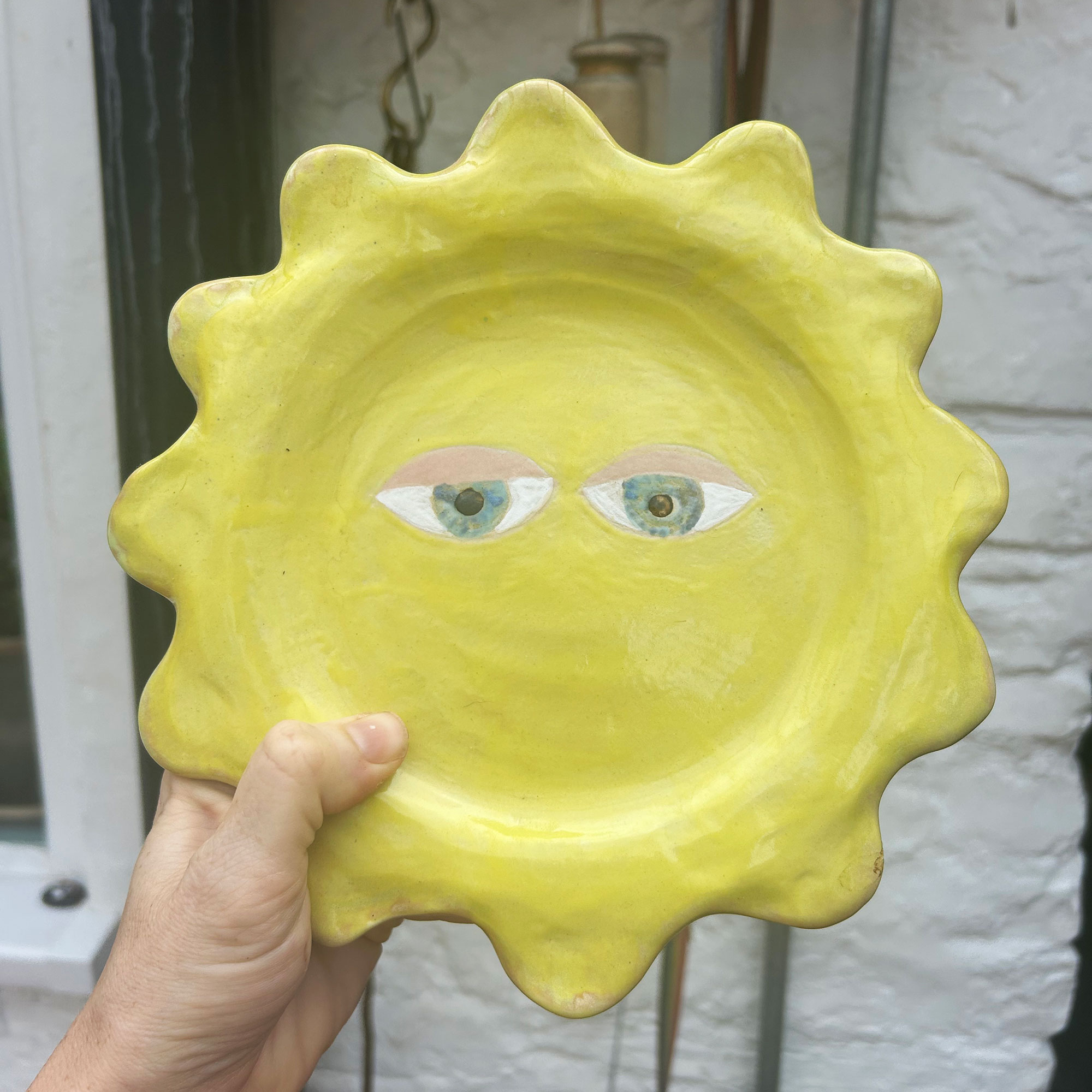Person holding ceramic yellow sun dish with eyes in centre