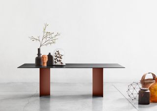 Dark coloured ‘Gullwing’ desk with contrasting legs against a light coloured background with various sculptures on top and beside it