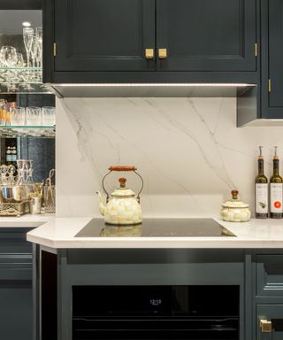 A blue-green kitchen with a build-in oven, a yellow and white kettle, and a home bar with a mirror behind