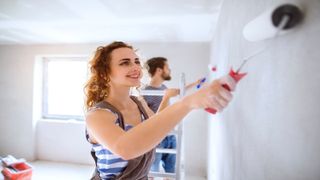 Woman and man painting home interior with rollers