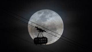 full moon shines behind a large cable car travelling across the face of the moon.