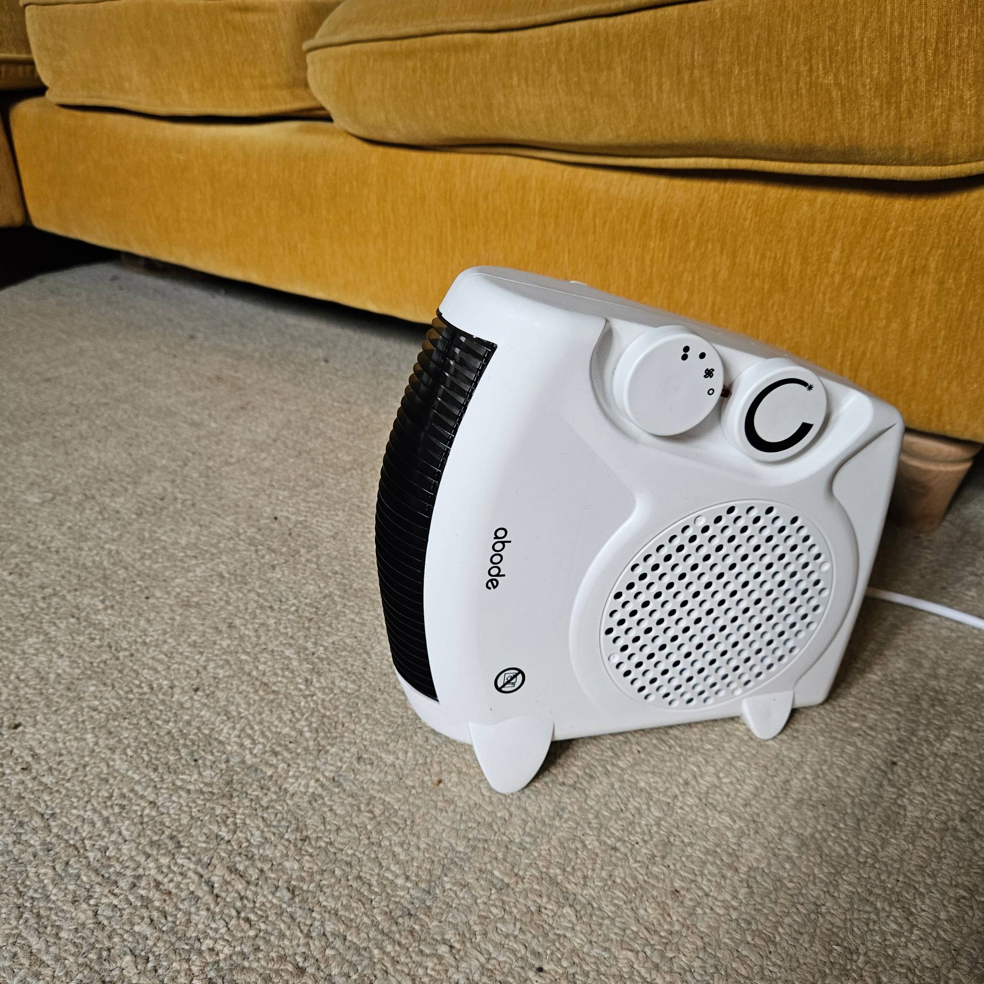 white Abode fan heater stood vertically next to yellow sofa