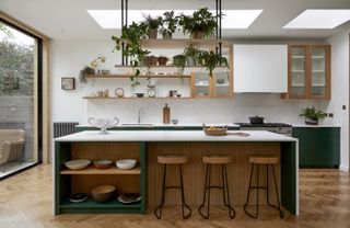 An open kitchen with open shelving and glass cabinets. Plants hang above the kitchen island creative a touch of elegance to the space.