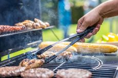 A person cooking burgers, chicken and corn on the BBQ.