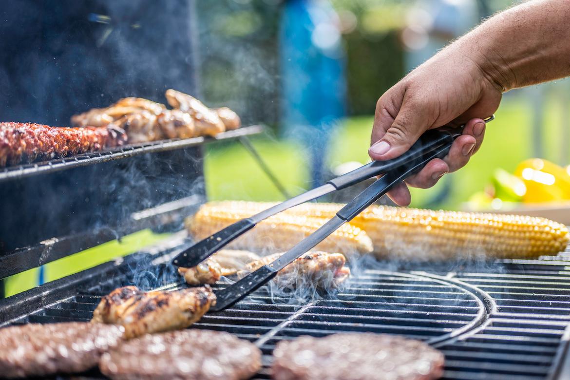 A person cooking burgers, chicken and corn on the BBQ.