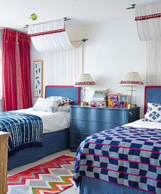 boys' bedroom with blue beds, blue patterned throws, red curtains and colorful rug