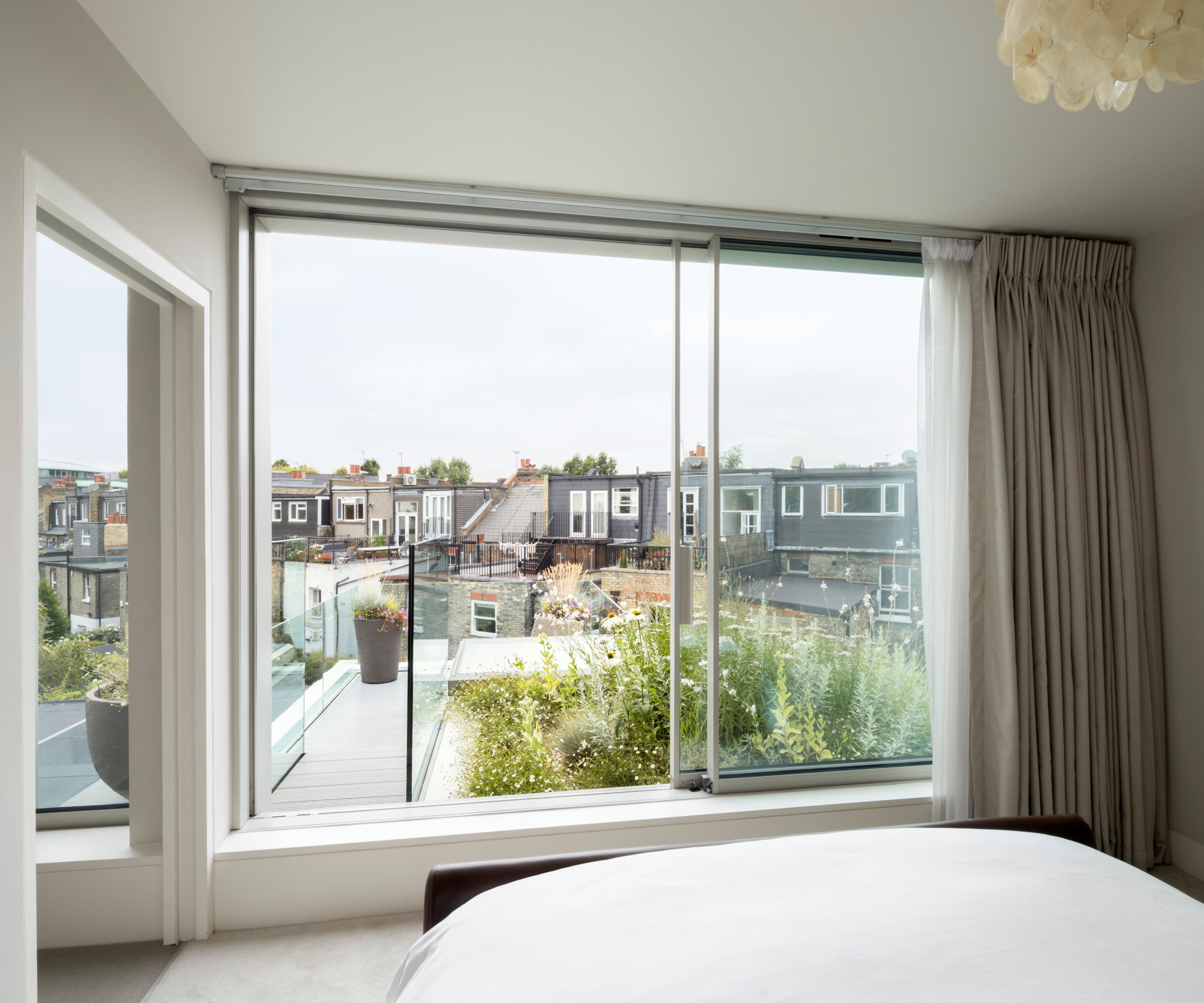 view from inside loft conversion bedroom to sliding glass doors leading out to roof terrace with glass balustrade and planted area