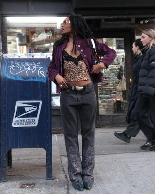 woman wearing leopard print camisole top, purple cardigan, gray printed jeans, Y2K era sunglasses