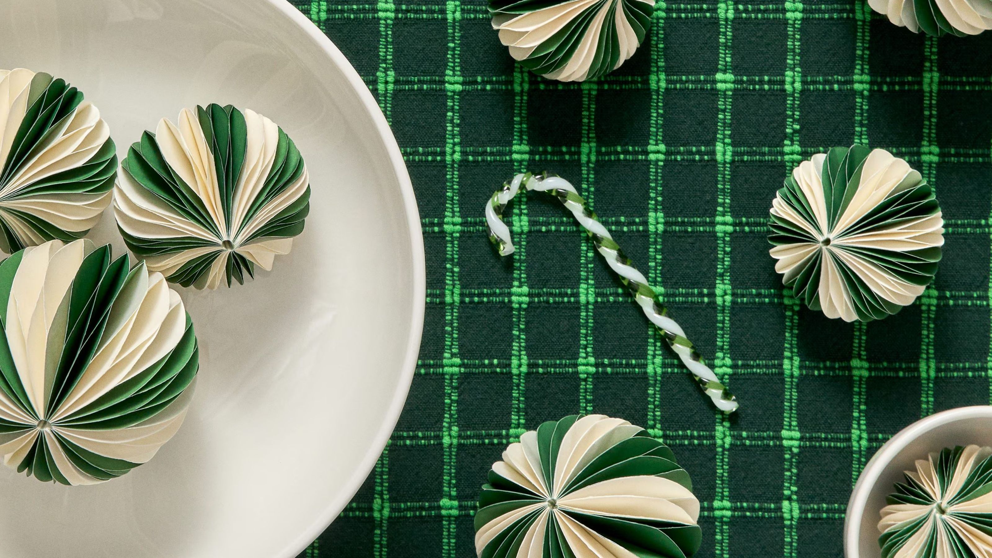 green and white paper Christmas baubles on a green grid-patterned tablecloth