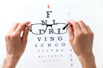 A pair of glasses held next to the diagram of the Snellen vision test