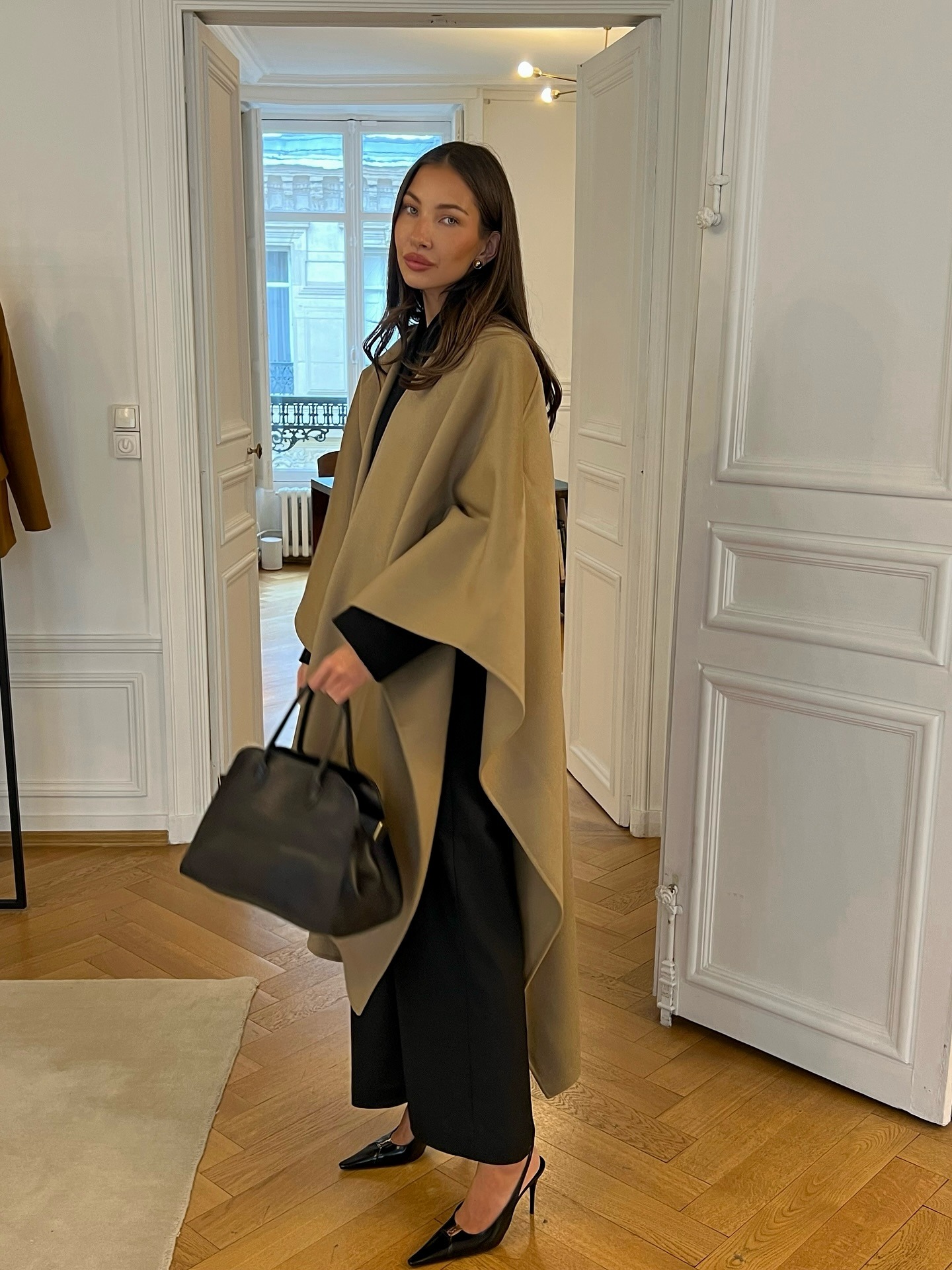 Influencer @fakerstrom wears a poncho jacket with black trousers, a black bag and black slingback heels.