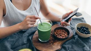 Woman drinking green juice and snacking on almonds in the morning