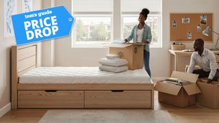 A student unpacking the Zinus Dorm 101 Ultimate Sleep Bundle in her dorm room while her father unpacks boxes, with a Tom's Guide badge overlaid saying "PRICE DROP"