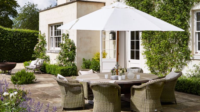An example of easy patio cover ideas showing a white parasol over an outdoor dining table and wicker chairs