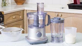 A food processor with blender pitcher on a kitchen countertop next to a bowl and sieve ready to make cake batter