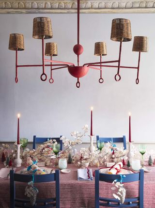 Red striped tablecloth with four blue chairs. There are green wine glasses, white floral pieces, and white candle holders with red candle sticks