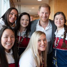 Prince Harry posing with women of Team USA wearing red, white and blue warm up suits at the 2025 Invictus Games