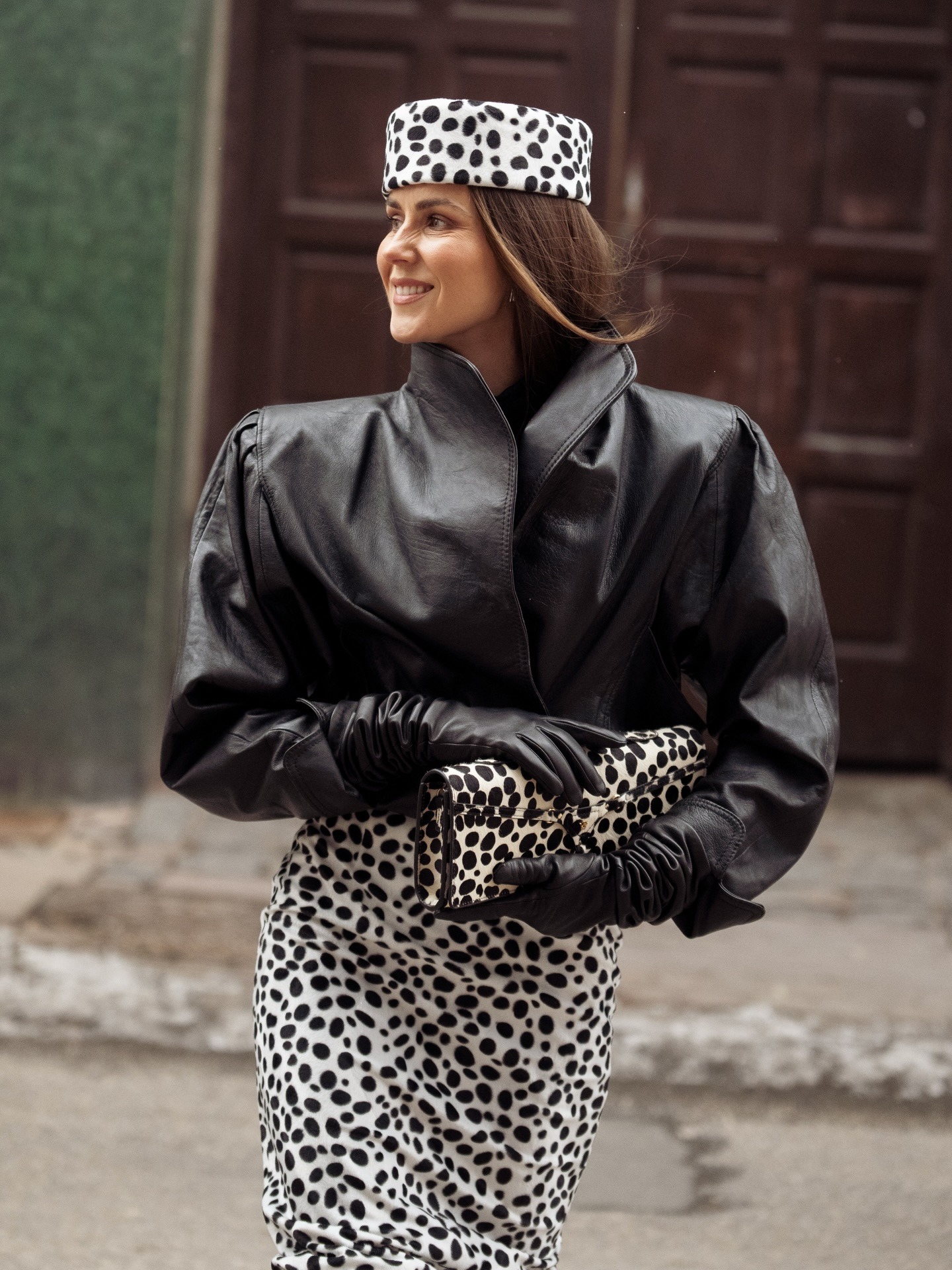 Woman wearing black leather jacket, dalmation print skirt, dalmation print clutch, and dalmation print pillbox hat.