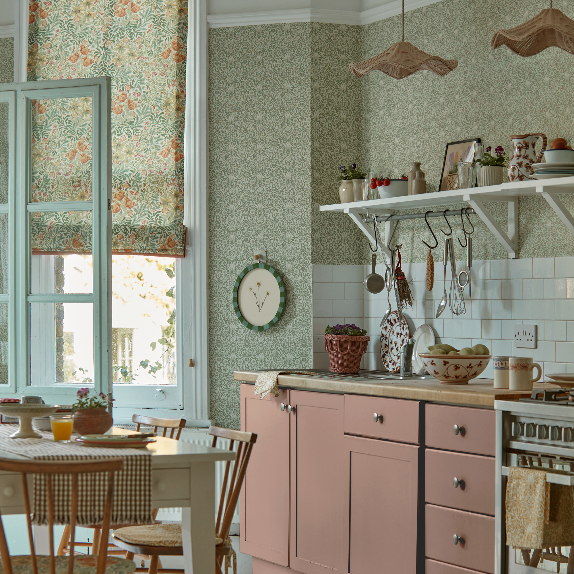 a pink painted kitchen with william morris print wallpaper and blind