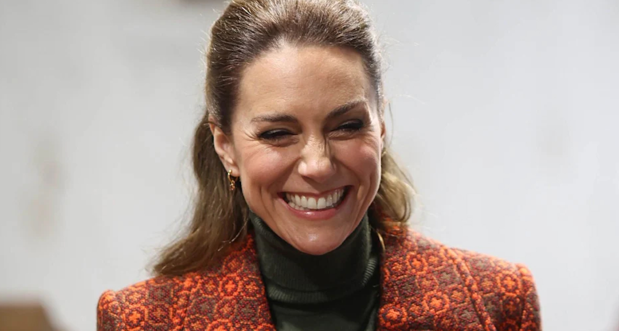 Kate Middleton wearing an orange coat and laughing