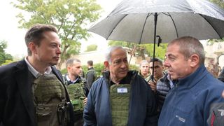 three men in combat armor stand under an umbrella, talking