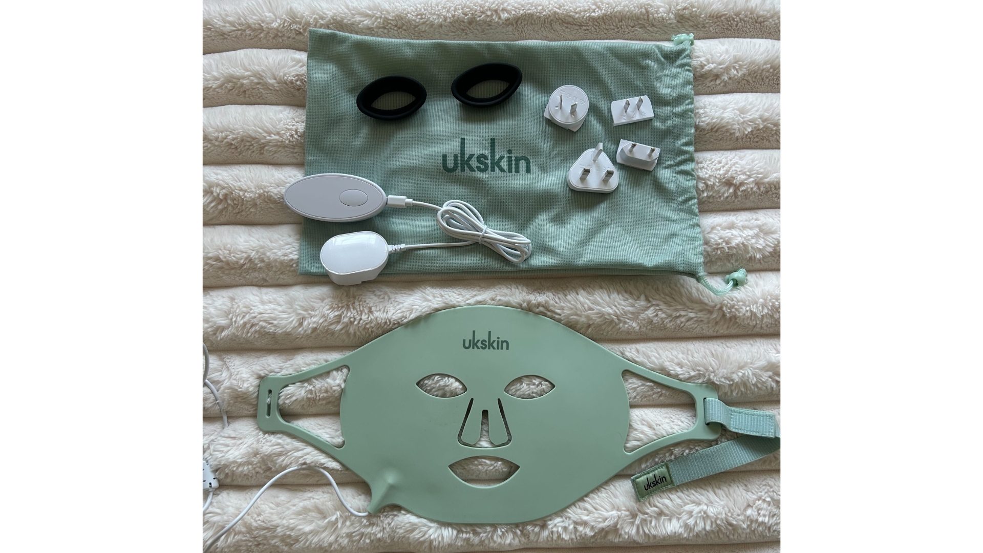 Image of mint green UKLASH LED mask laid out showing the travel bag, eye protectors, charging cable and four travel plug adaptors