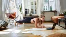 Woman doing a plank pose at home in front of laptop.