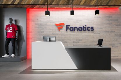The Fanatics logo on the wall of an office next to a mannequin dressed in sportswear